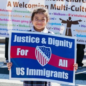 A child holds a sign that says "Justice & Dignity for all US Immigrants"