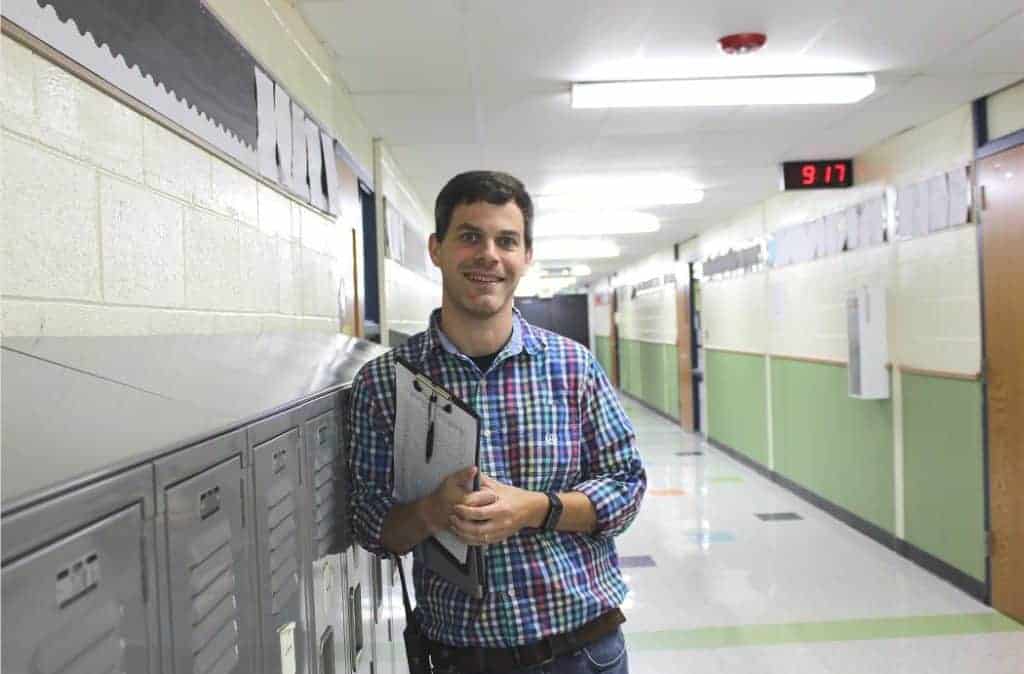 Principal Bryan Gibson leans against a locker in a school hallway
