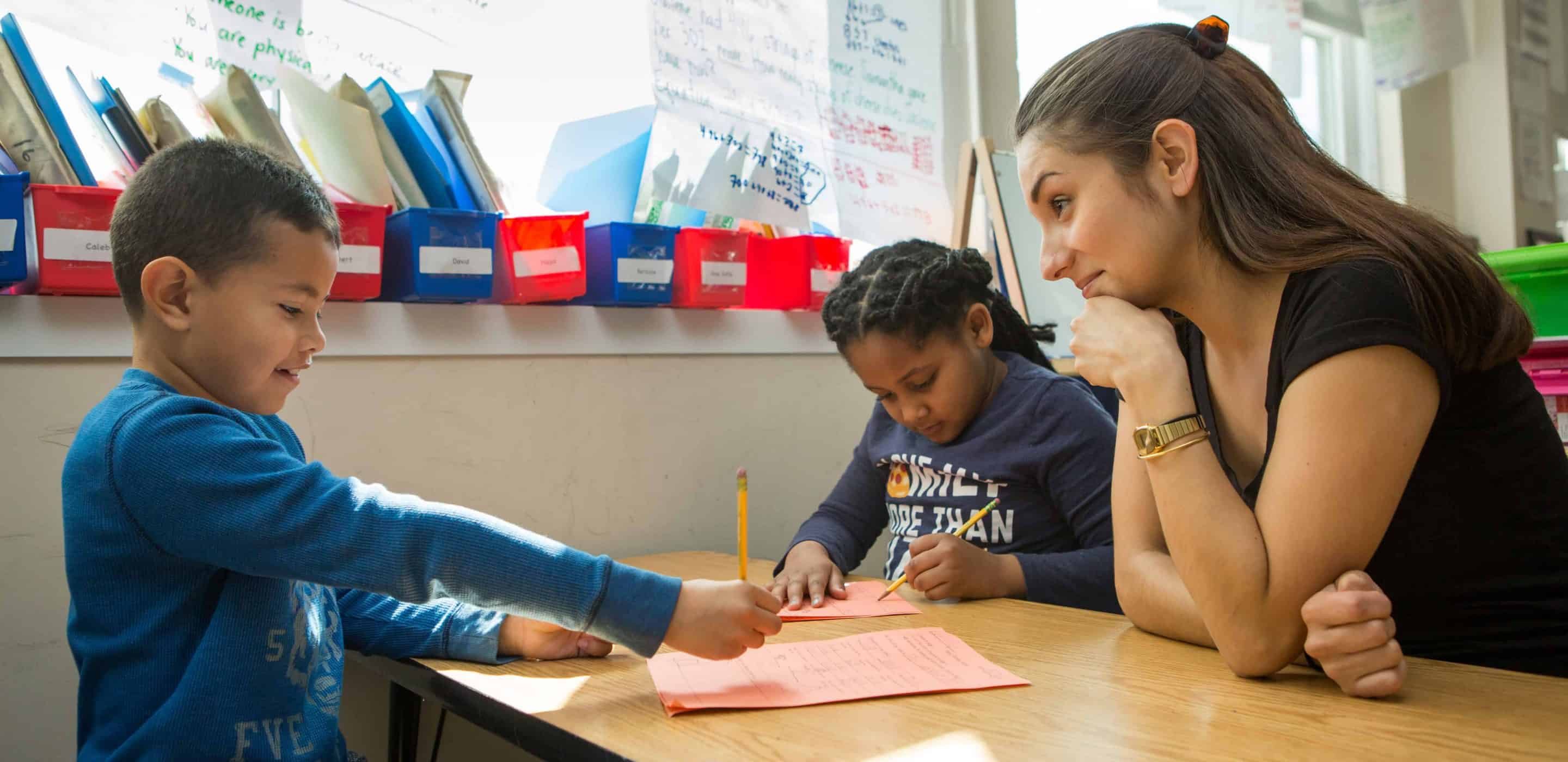 A teacher at Capital City PCS looks on as two students write