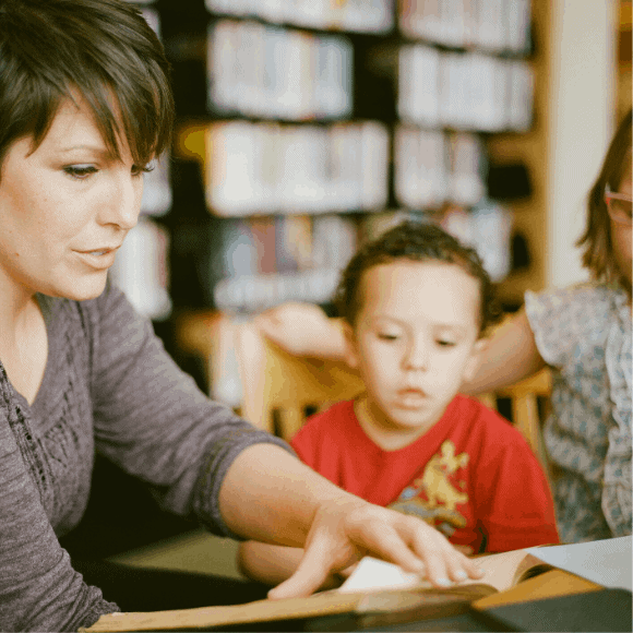 a woman reads to two children in a library