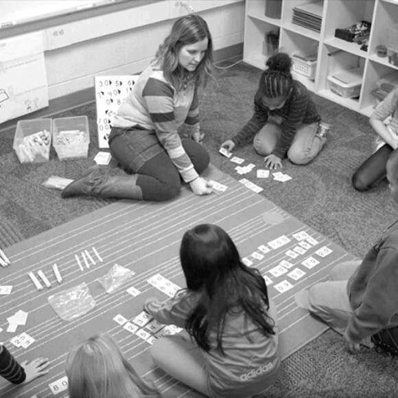 a grand rapids educator sits on the floor with a group of students