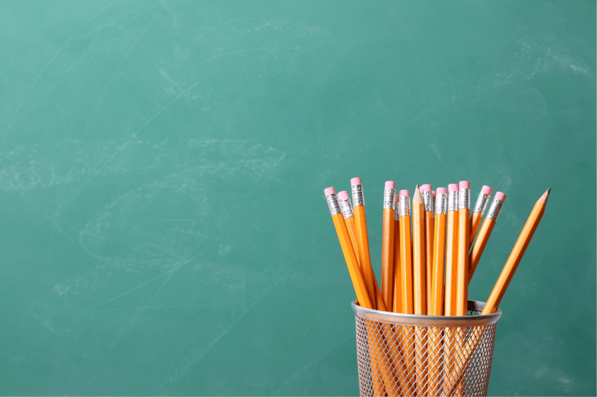 A canister of orange pencils in front of a green chalkboard