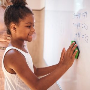 a girl does a math problem at a white board