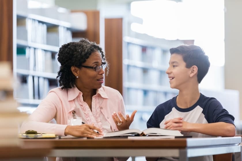 a teacher talks to a student at a table in the library