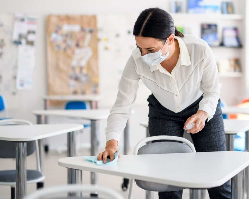 a teacher wipes down a desk