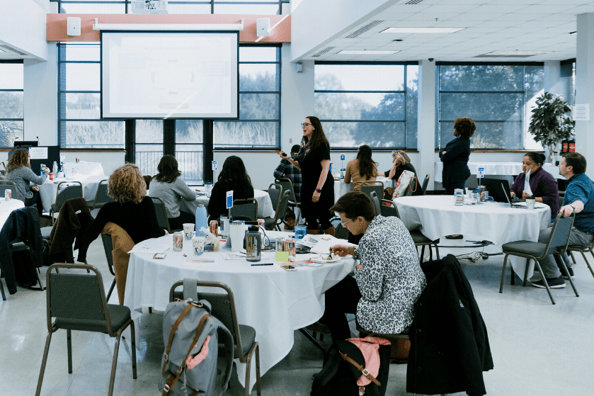 a woman presents to a group of teachers seated around round tables