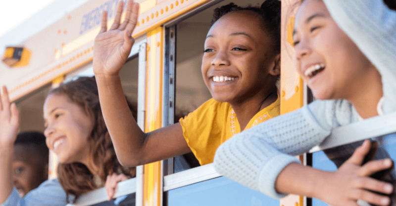 diverse kids waving their hands out the windows of a yellow schoolbus