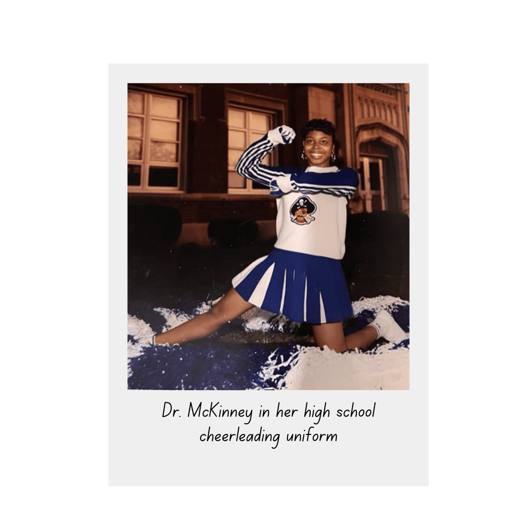 A high school girl poses in front of her school in a cheerleading uniform